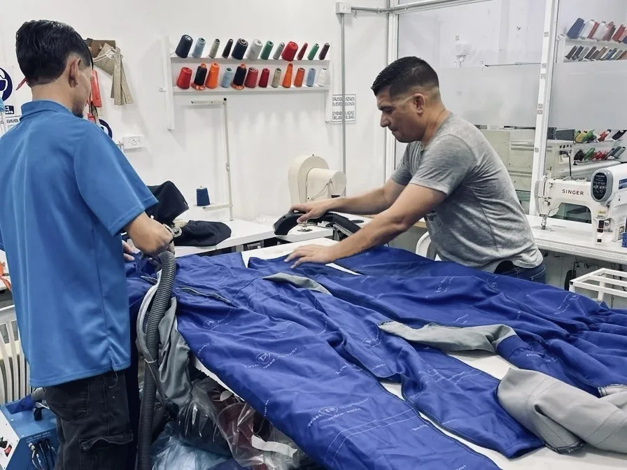 Dos operarios revisando un overol azul terminado sobre la mesa.